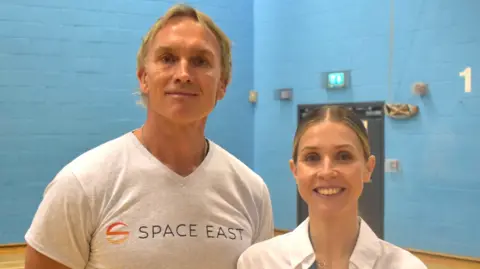 Suffolk New College Matt Bagley standing next to Kayleigh Norris. Matt is wearing a grey T-shirt with Space East written on it and Kayleigh is wearing a white shirt. They are both smiling and looking into the camera.