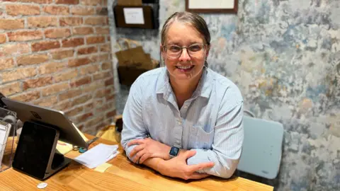 Woman with glasses in blue striped shirt stands behind wooden standing desk 
