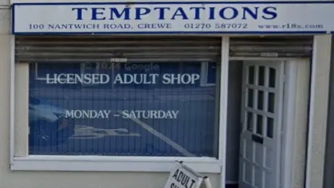 The front of a shop, with the name Temptations across the top, and the words licensed adult shop across the partially shuttered front window.