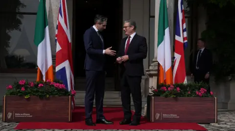 PA Media Prime Minister Sir Keir Starmer speaking with Taoiseach Simon Harris. There are Irish and Union Jack flags on either side of the two leaders. They are standing outside Farmleigh House in Dublin.