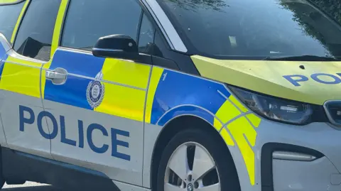 A police car with blue and fluorescent yellow markings and the word "police" in blue. A shield with the words Guernsey Police is on the door.