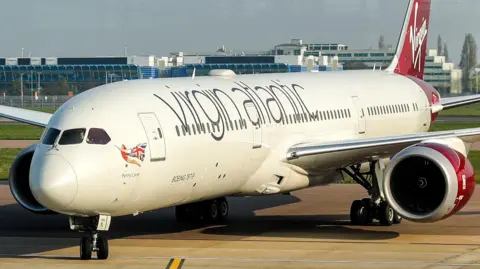 PA Media A white plane with red engines and tail, with a Scarlet Lady mural on the front