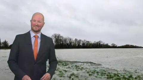 Darren Bett standing in front of an image of a snowy field with grey sky behind