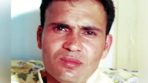 Family A man with short, brushed black hair sitting on a floral sofa and looking at the camera.