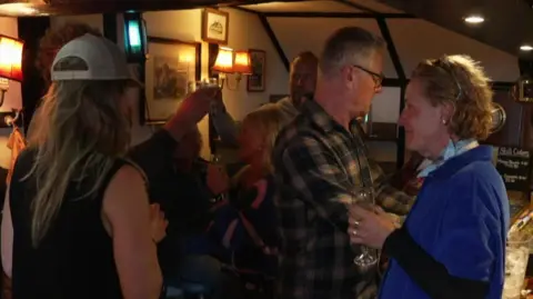 People stand by a bar at a pub with drinks in their hands as they celebrate good news.