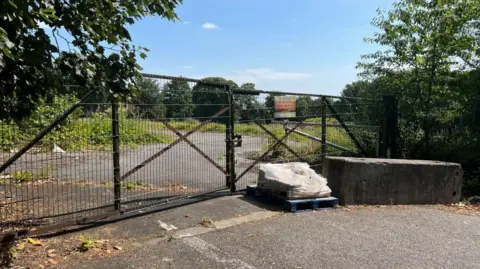 Aisha Iqbal/BBC Locked gates in front of a patch of scrap land. It is a sunny day