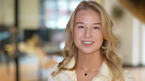 Jamie Niblock/BBC Alice Davis, in an office. She has shoulder-length curling blonde hair and is wearing a white shirt. 