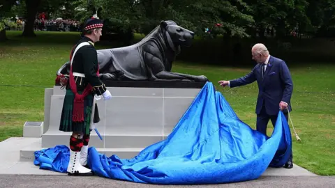Getty Images The King and a soldier in full ceremonial dress, unveil a statue of a lion.