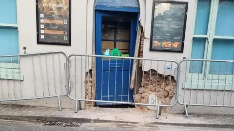 BBC The entrance to the pub fenced off, with the wall and door damaged.