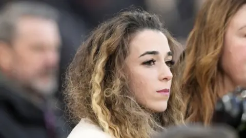 PA Media Jota's wife, wearing a white coat, looks out from the stands at Anfield as her two sons lead tributes to the Portugal forward