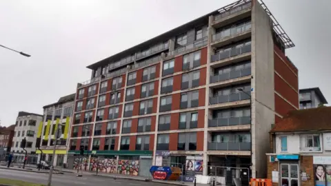 Red brick block of apartments in High Street, Slough, with seven floors about a row of shops.