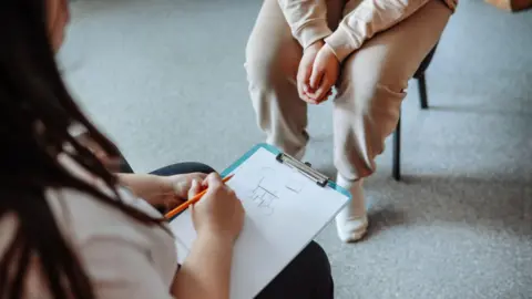 Psychologist makes genogram on clipboard while counselling teenage girl.