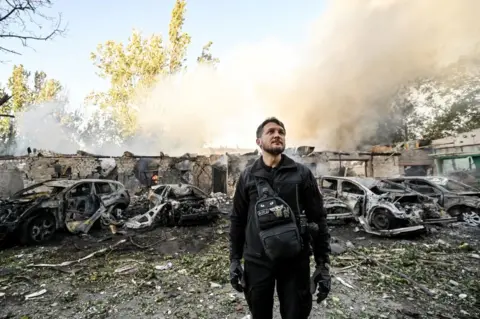 Getty Images Un hombre aparece frente a los coches destruidos por el bombardeo ruso.