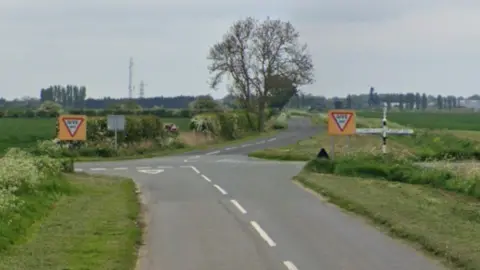 Google shot of the Fulney Drove and Mill Drove North junction. Two give way signs are visible in the image, along with a black and white toad sign. There is a tree in the background.