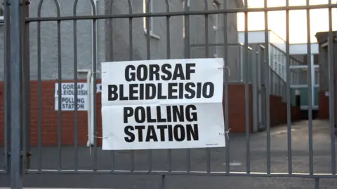 A sign that reads "polling station" in English and Welsh, with the Welsh "gorsaf bleidleisio" written at the top of the sign. It is attached to railings in front of a building that looks like it could be a school or another municipal institution.
