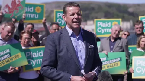 Rhun ap Iorwerth stood in front of a crowd holding Plaid Cymru banners