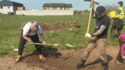 Archaeologists in a field with axes digging.
