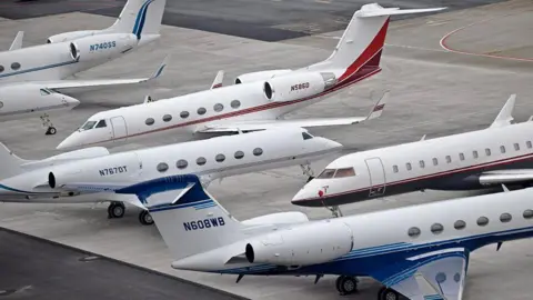 Generic image of several white private jets on the ground at an airport