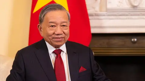 Getty Images Tô Lâm sits in front of a Vietnam flag