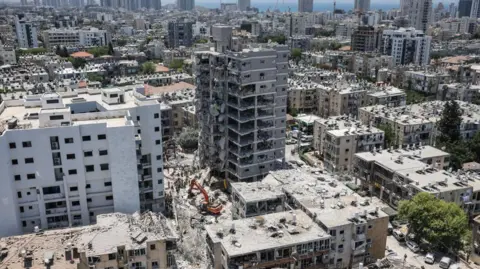 A landscape image of a residential areas where buildings have been damaged and rubble lies on the ground.