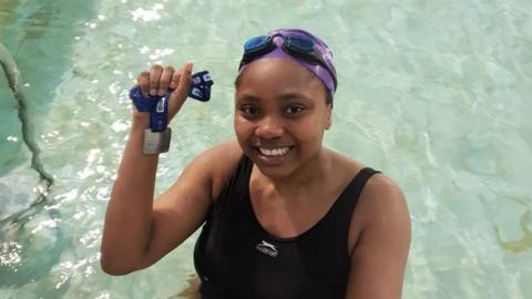 Woman holds up a medal in swimming pool