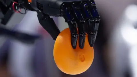 A robot hand holds an orange ball