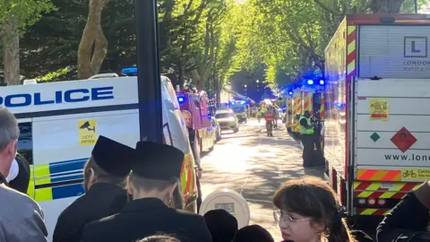 People stand near a cordon and some emergency vehicles
