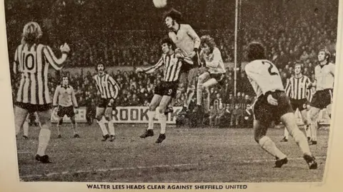 Nicola Haseler/BBC A black and white photograph from the 1970s shows Walter Lees jumping in the air to head to ball while two other players challenge him