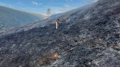 Derbyshire Fire and Rescue Service A firefighter damping down hot spots following a moorland wildfire on Tintwistle Moor, above Woodhead Road in Glossop, Derbyshire.