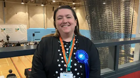 Lindsay Green in a blue rosette looks into the camera