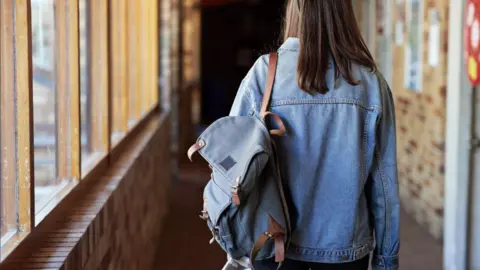 Getty Rear view of young woman with backpack (rucksack or satchel drapped over shoulder) walking in corridor
