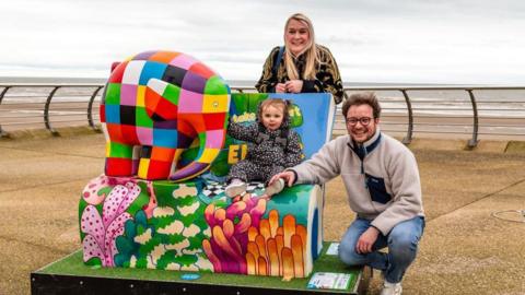 A family posing at the Elmer book bench in Blackpool during the trail 