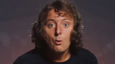 Jasper Carrott, with curly hair, wearing a black T-shirt.