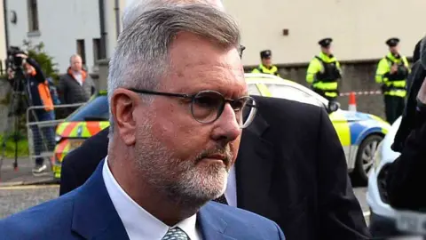 EPA Sir Jeffrey Donaldson wearing black spectacles, a blue suit and green tie arriving at court