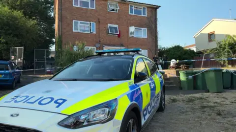A police car in front of a cordon at a crime scene
