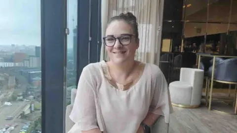 Natalie-Anne Rowlett Natalie-Anne has dark brown hair and glasses and is sitting in a restaurant in this photo.