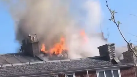 Fubar News Flames coming through the roof of a building.