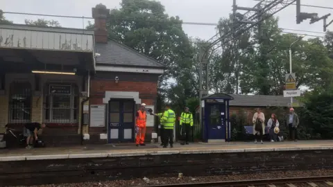 Police and railway engineers talk to commuters on the platform at Poynton railway station
