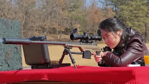 KCNA Kim Ju Ae, wearing a maroon leather jacket, shoots a sniper rifle