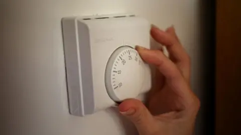 PA Media A woman's hand turns a thermostat dial.