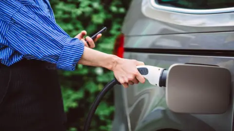 A woman in a blue shirt plugs a charger into her electric vehicle