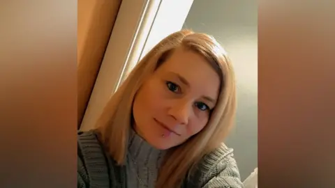 Samantha King A selfie of Samantha King. She has blonde hair and a piecing below her bottom lip. She is wearing a green knitted jumper.