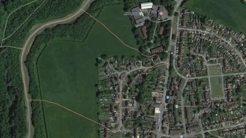 A satellite image of a village. To the west is an area of green space with a computer-generated line around it, indicating where new homes will be built.
