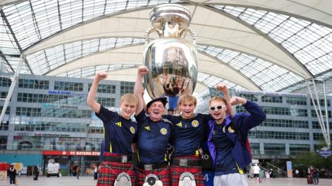 Scotland fans dressed in kilts pose in front of a replica of the Euro 2024 trophy