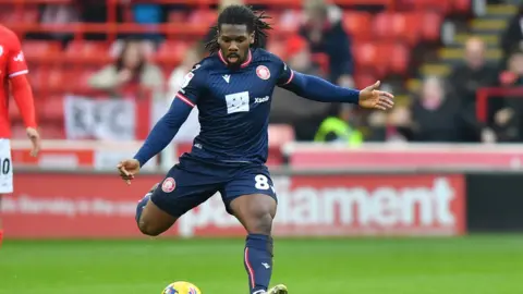 Stevange midfield Dan Phillips goes to kick the ball in away blue kit