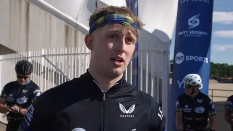 BBC/Stuart Prandle Hamish Weir, who is wearing a black tracksuit and tartan headband, is speaking to a reporter who is out of the shot. 