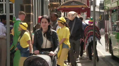 A woman pushes a pram while Gru, from the Minions film, walks behind her
