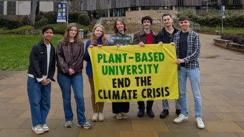 Students stood outside the University of Southampton holding a yellow green and black banner which reads: "Plant-Based University End the Climate Crisis".