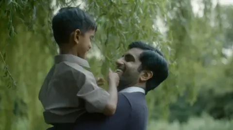 Amar Singh Sethi The lead character of Bus Driver lifting up his son in a picturesque, wooded area. Both are smiling, and enjoying the moment.