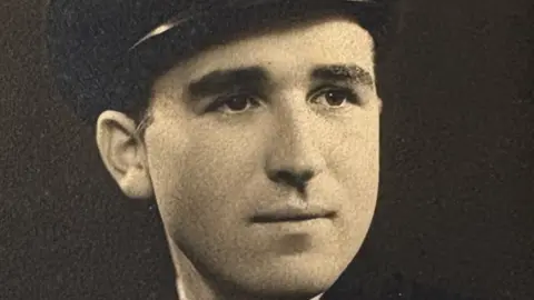 A black and white photo of a young man in military uniform. He is wearing a cap.